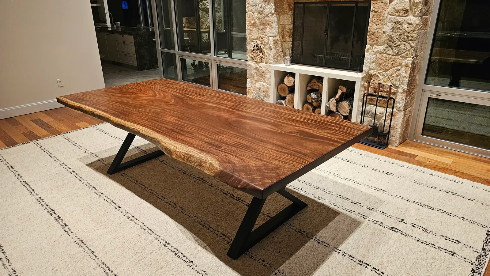 Live edge dining table with metal base in open living space with stone fireplace
